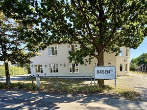 Basen Vest i Taastrup set fra gaden. En lysegrå bygning med træer foran og blå himmel.