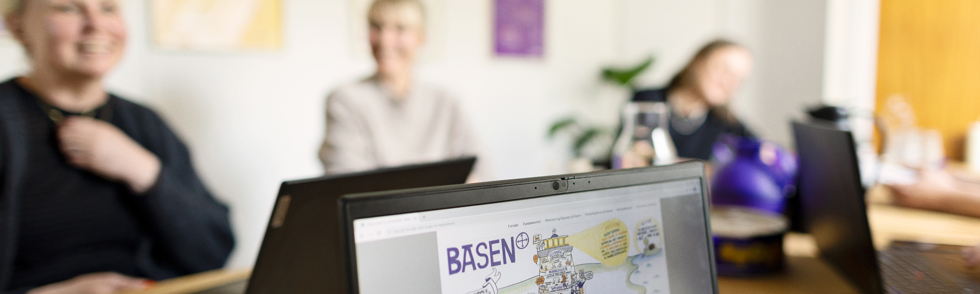 En computerskærm med tekst på og tre mennesker i baggrunden