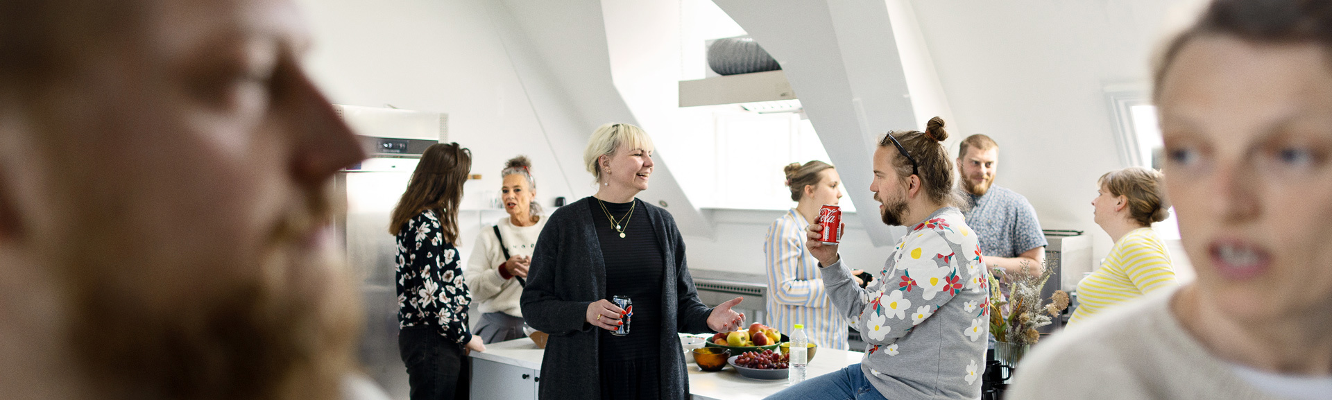 En gruppe mennesker der taler med hinanden i et hvidt køkken - to af dem ses i forgrunden