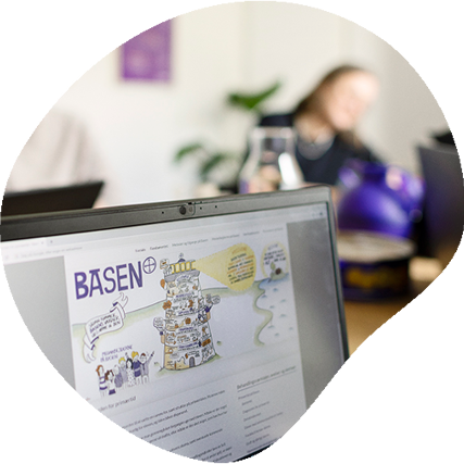 PC i forgrunden med Basens logo og fyrtårn på skærmen