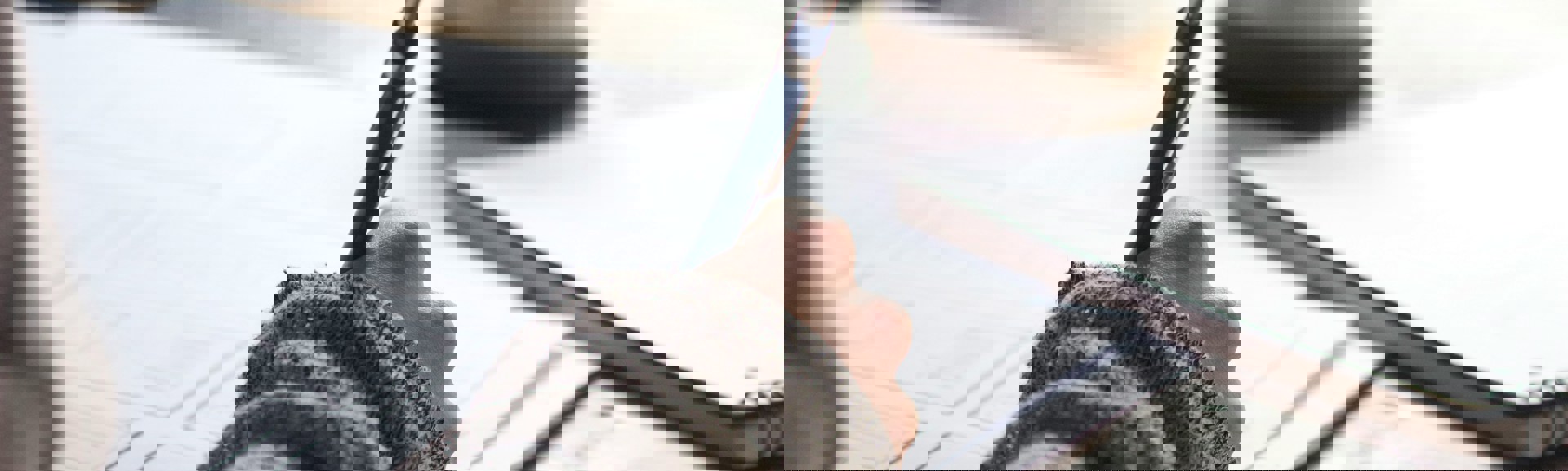 et udsnit af en person med en kuglepen i hånden der skriver og en kaffekop i baggrunden