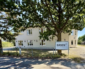 Basen Vest i Taastrup set fra gaden. En lysegrå bygning med træer foran og blå himmel.