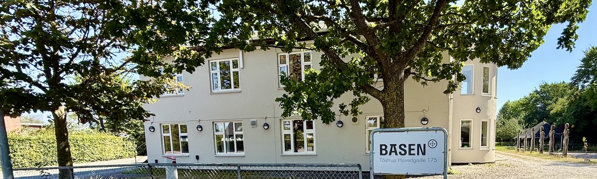 Basen Vest i Taastrup set fra gaden. En lysegrå bygning med træer foran og blå himmel.