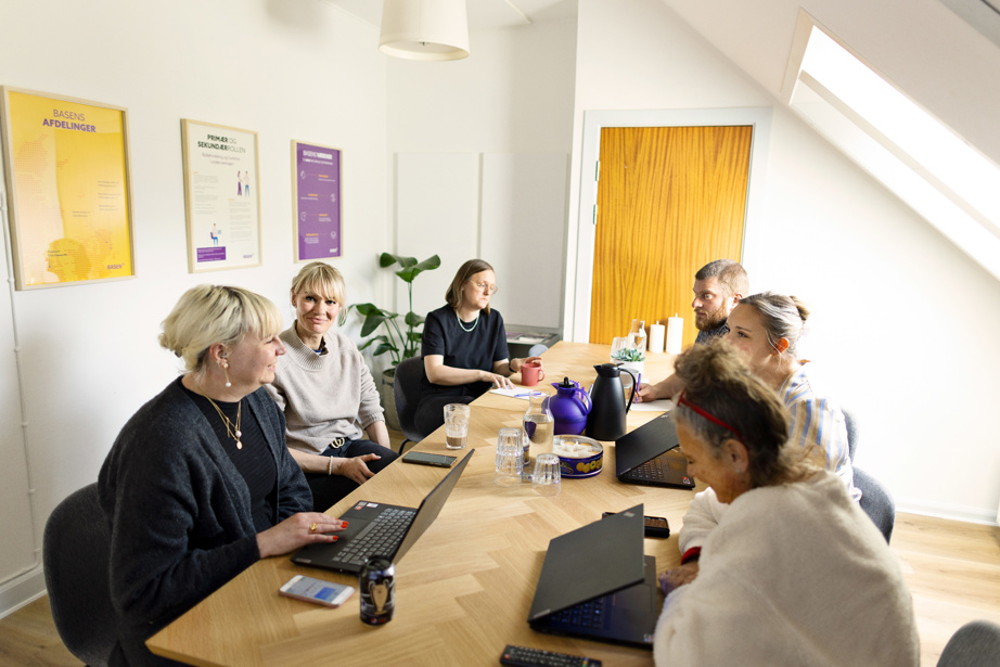 Seks mennesker der sidder omring et bord og taler sammen