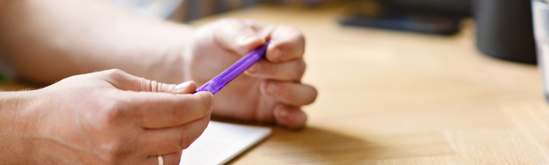 To hænder der holder en kuglepen ved et bord.