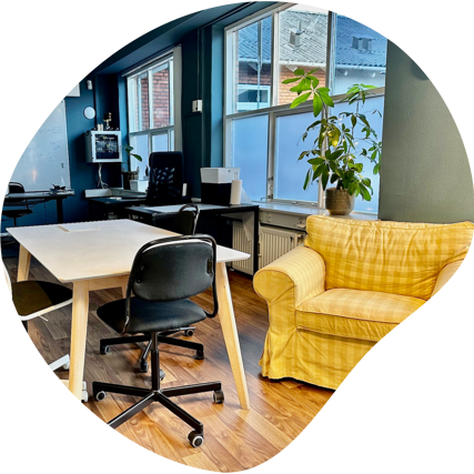 Udsnit af klasserum med borde, stole og en gul lænestol.