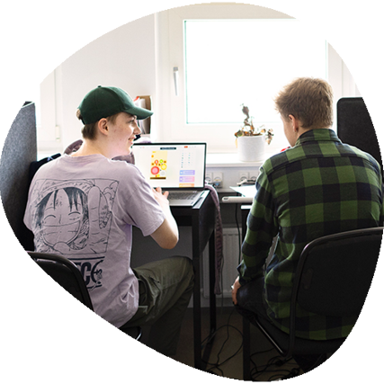 To elever der sidder ved skærmede pladser i klasselokalet og taler sammen.