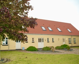 Billede af Basen Fyn på Thulevej i Odense. En gul bygning med rødt tegltag omgivet af en græsplæne og et grønt tag.