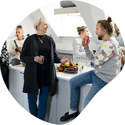 5 voksne mennesker samlet i et hvidt køkken mens de taler sammen 